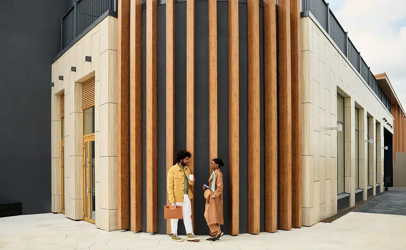 Zwei Personen unterhalten sich vor einem modernen Gebäude mit Holzlamellen