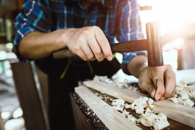 Person schlägt mit einem Hammer einen Nagel in ein Holzbrett